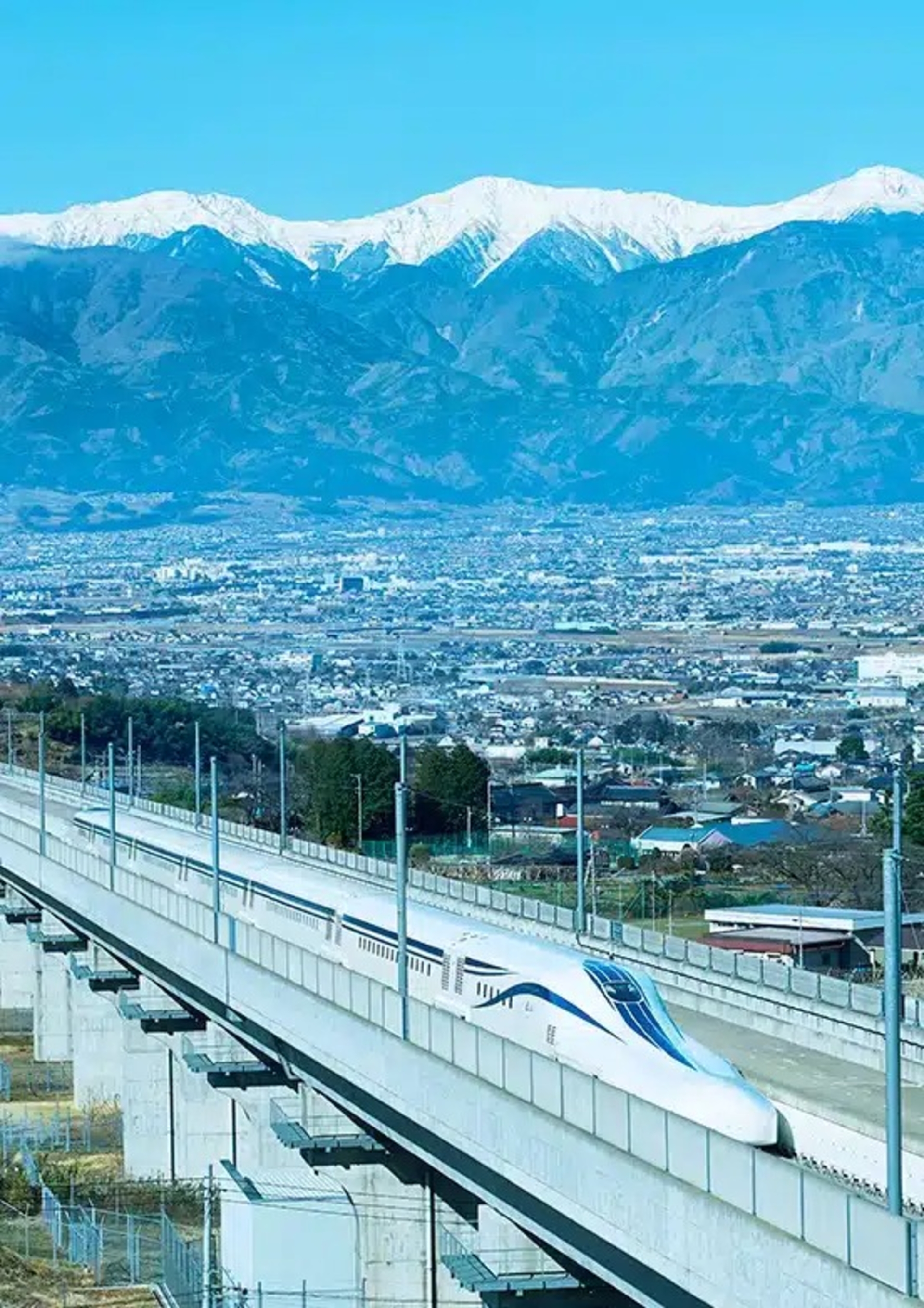 قطار برقی مگلو ژاپن روی پل در حال حرکت در پس‌زمنیه‌ی شهر